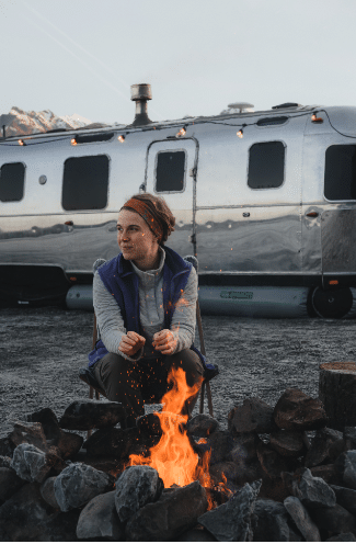 lady warms in front of fire travel trailer with rv skirting in background